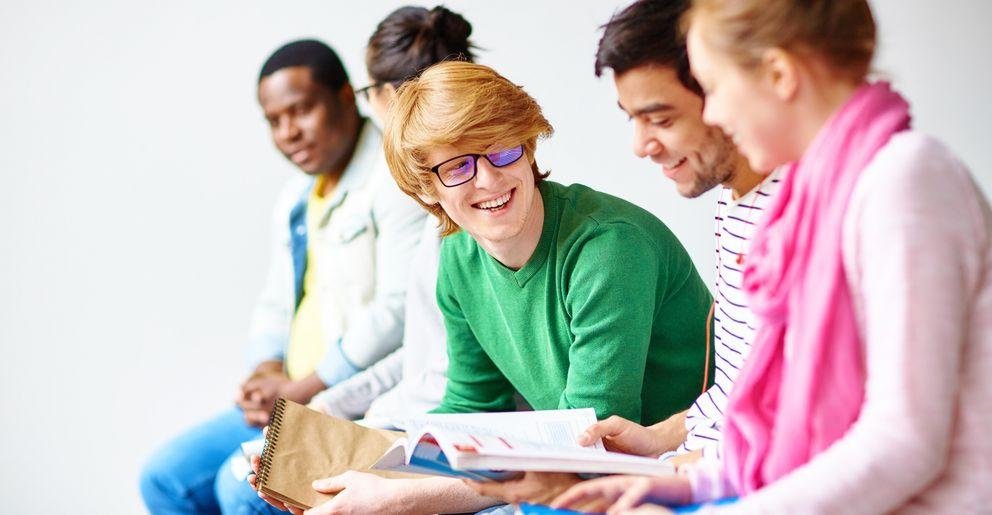 Studentengruppe Fünf Studenten sitzen in einer Reihe und sprechen lächelnd miteinander.