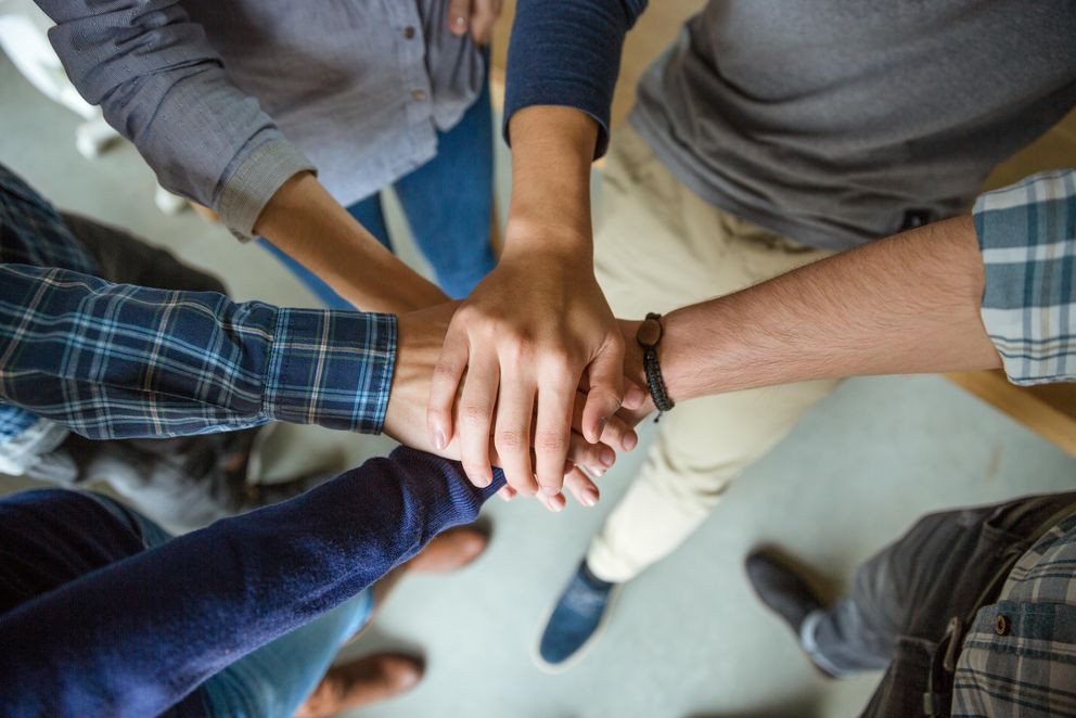 A group of people form a circle and place their hands over each other in their center.